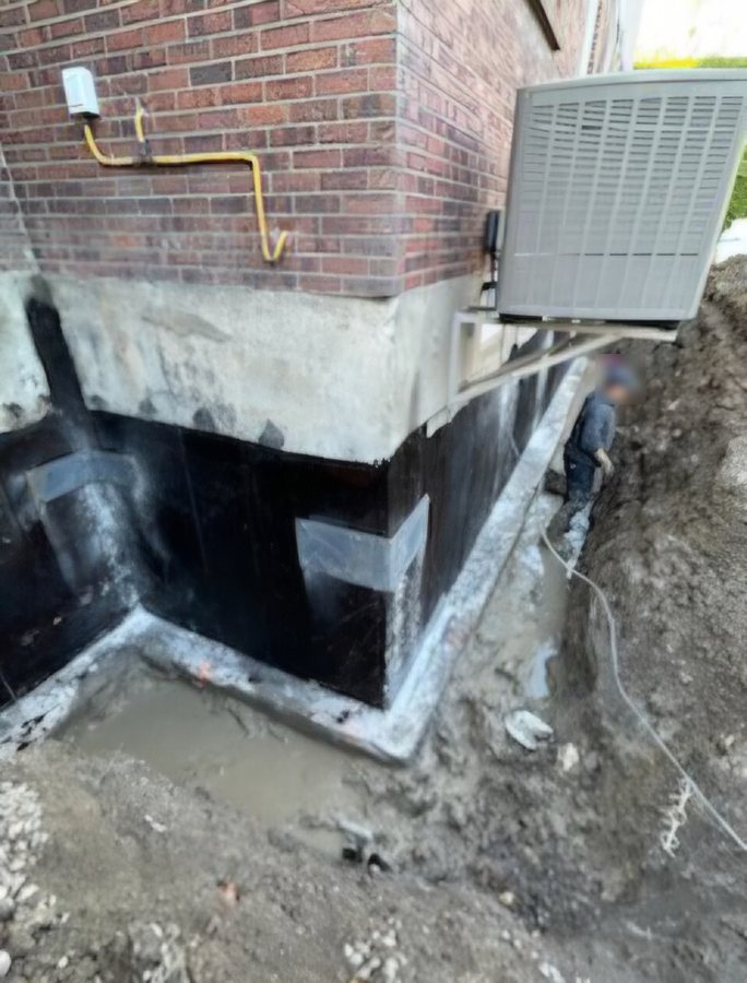 Membrane noire et bandes de renfort aux coins de la fondation, tranchée prête pour le drain français.