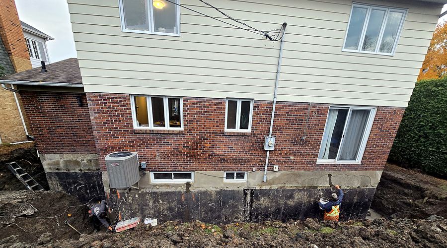 Fondation dégagée et membrane d'imperméabilisation sur tout le mur.